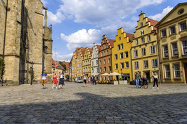 Osnabrücker Marktplatz mit Giebelhäusern bei sommerlichem Wetter. Im Hintergrund sind Personengruppen zu sehen, die über den Marktplatz laufen.
